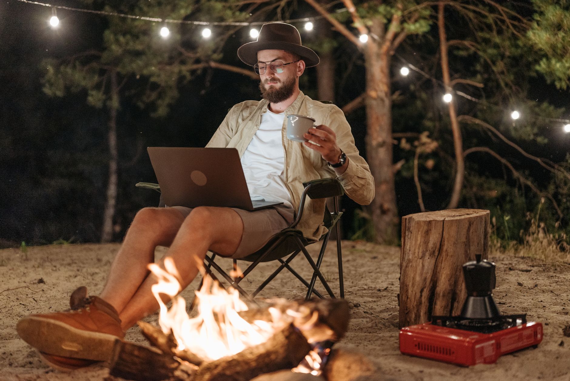 man sitting with a laptop by a bonfire on a beach