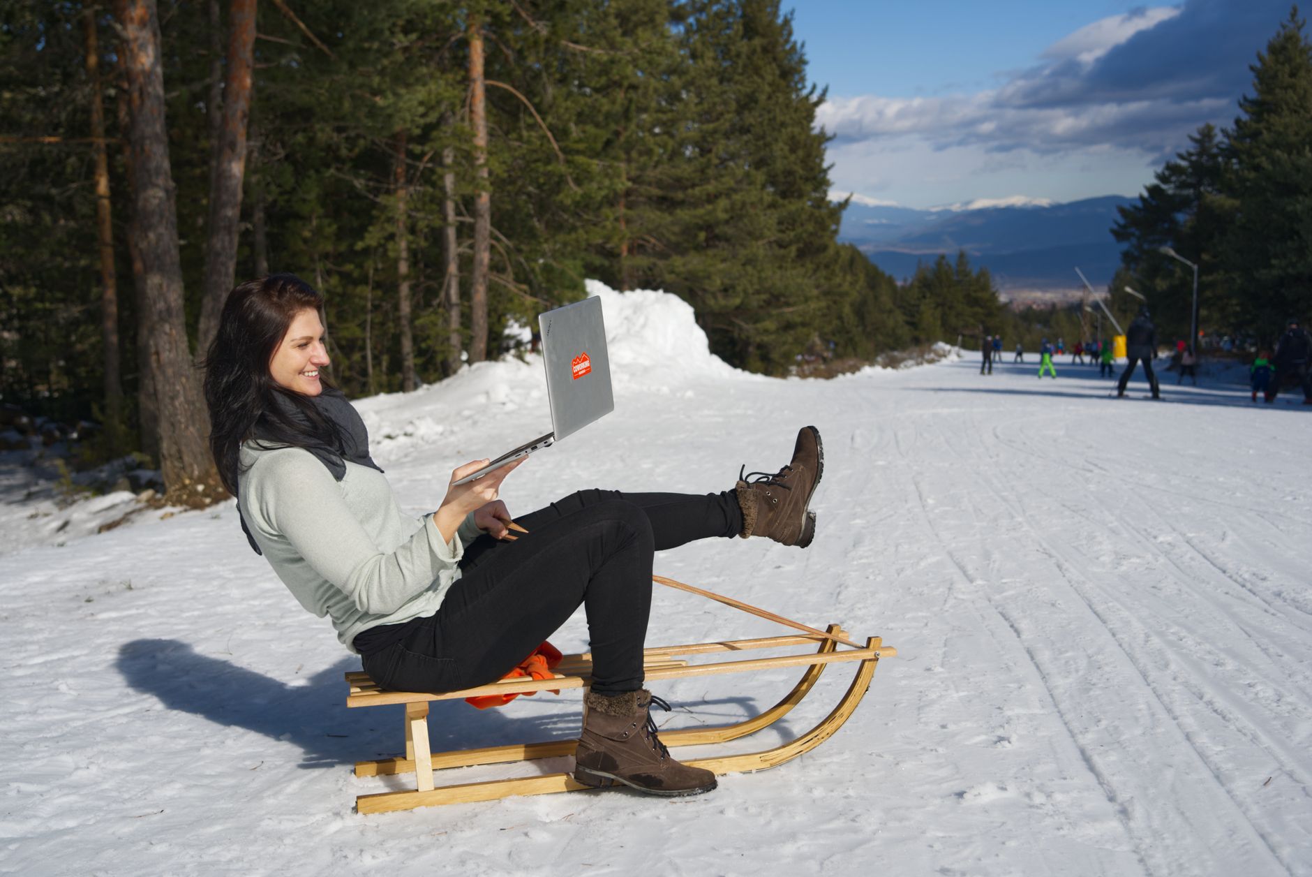 woman sitting on wooden sled using silver macbook