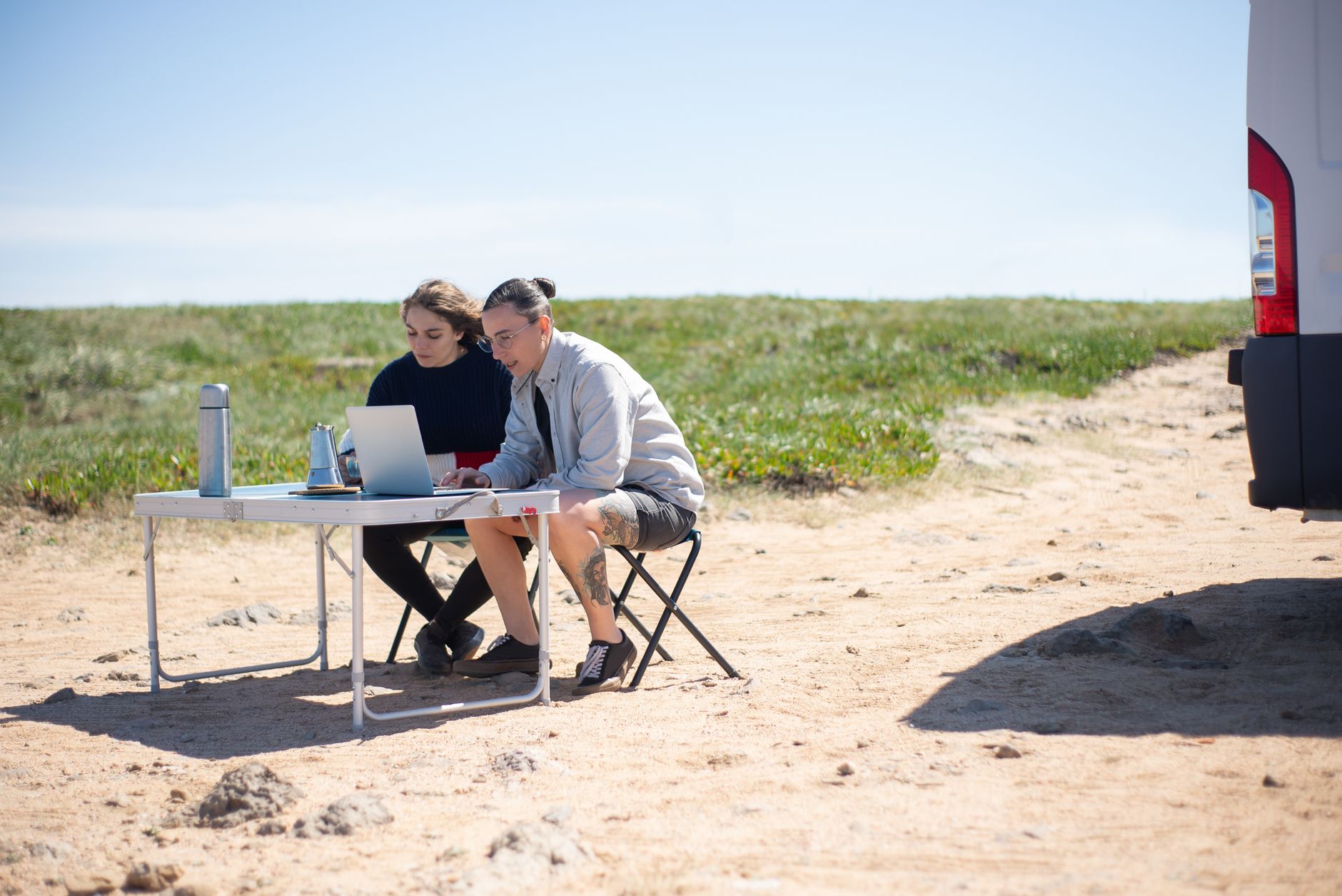 women by table with laptop near car